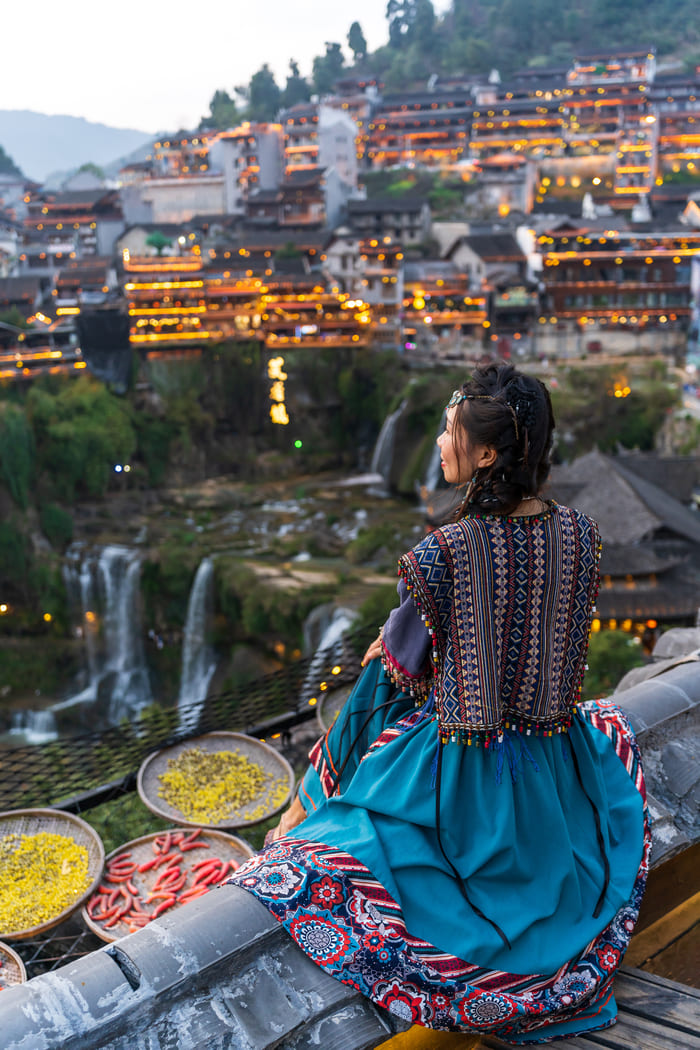 Viajera contemplando un pueblo tradicional de China con cascadas y luces al atardecer